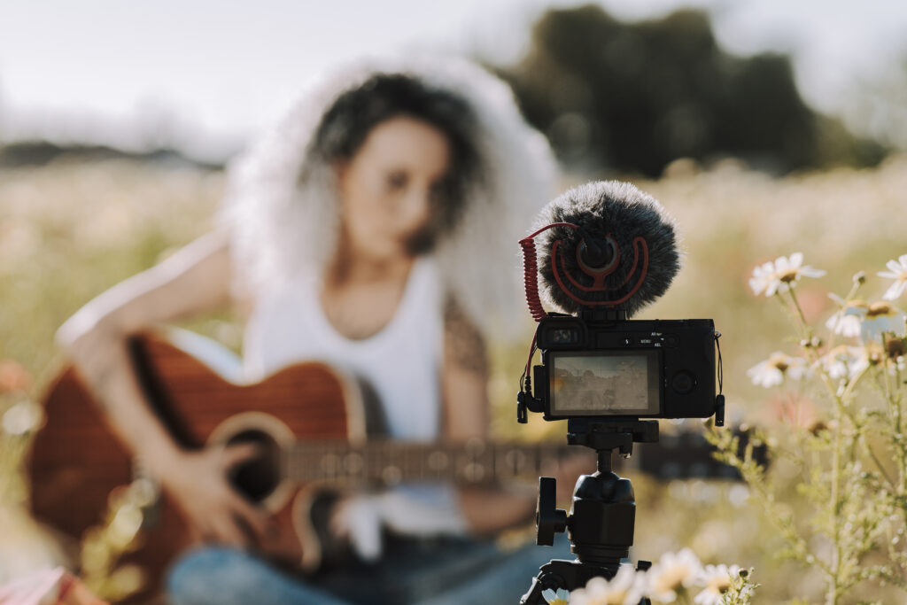 Curly-haired Spanish cute woman playing guitar in a field of daisies while recording a vlog